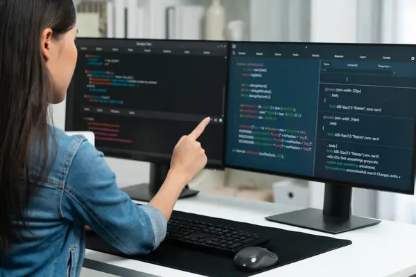 Young Asian girl of IT developer pointing online information on pc with coding program data application on website project, wearing jeans shirt. surrounded by safety programing two screens. Stratagem.