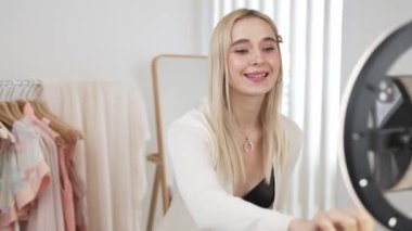 Genç sosyal medyum kadın moda videosu yapıyor. Blogcu kameraya ve ışık çemberine gülümserken, aynı zamanda ikna edici çevrimiçi kıyafetleri izleyicilere veya takipçilere vlog sattırıyor. Blithe