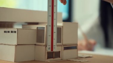 Cetvel ölçü evi modelini kullanan yetenekli profesyonel mühendis elini kapatırken, genç yetenekli mimar da taslak çiziyor. Yaratıcı ve profesyonel tasarım. Eline odaklan. Tertemiz..