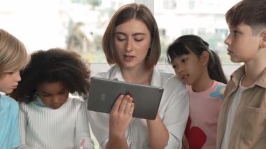 Bir grup öğrenciye çevrimiçi ders verirken elinde tablet tutan akıllı öğretmen. Yetenekli eğitmen mühendislik derslerini anlatırken genç öğrenci oturuyor ve sunumu dinliyor. Etkinlik.