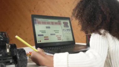 Dizüstü bilgisayar kodu gösterilirken Afrikalı kız yazma ya da araba modeli yapısı. BTMM sınıf çalışmalarında dizüstü bilgisayar geliştirme programı ya da programlama mühendisliği ile çalışan zeki öğrenci.