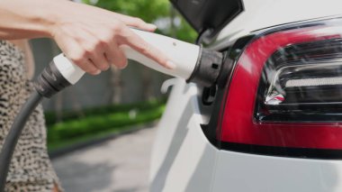 Genç bir kadın yazın yeşil sürdürülebilir şehir bahçesinde EV elektrikli arabasıyla seyahat ediyor. Kentsel sürdürülebilirlik yaşam tarzı yeşil temiz yeniden şarj edilebilir enerji elektrikli BEV araç iç organları