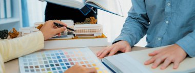 Proje yöneticisi toplantı masasında ev modeliyle ana tema rengini seçerken profesyonel iç tasarım ekibinin kırpılmış görüntüsü proje için renk ve malzeme kullanımı hakkında tartışır. Değiştirilmiş.