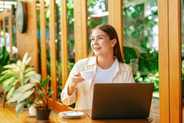 Genç bir kadın baharda açık kafe bahçesinde dizüstü bilgisayarda çalışıyor, kafeteryadaki huzur ortamının tadını çıkarıyor. Uzaktan çalışan ya da blog yazan dijital göçebe ya da üniversite öğrencisi. Yararlı