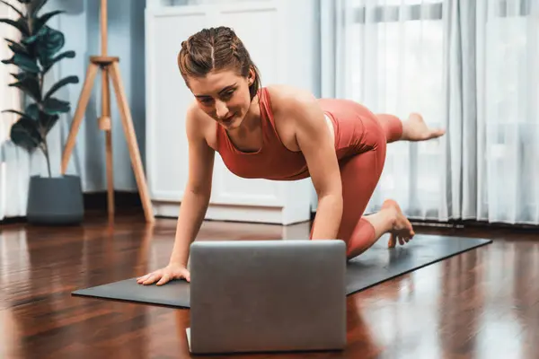 在家里锻炼垫子时 穿着运动服的灵活而敏捷的女人在冥想的姿势下做瑜伽 健康快乐家庭瑜伽在线培训课程 心平气和 — 图库照片