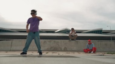 Bir grup Asyalı break dansçı, çok kültürlü arkadaş desteği ve hareketli hip hop müziğiyle sokak dansı yaptılar. Çekici yakışıklı hippi sokak dansında break dansçı. Açık hava sporu 2024. Yumuşak bir şekilde..