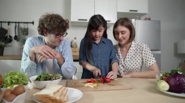 Çekici beyaz anne ve baba Asyalı kızıyla taze yemek pişirmek için birlikte vakit geçiriyorlar. Enerjik anne ve baba mutfakta salata yapmak için taze sebze hazırlıyor. Sağlıklı yiyecekler. Pedagoji.