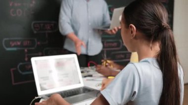 Afrikalı erkek manken tamir ederken beyaz kız programlama ya da kodlama sistemi. Öğretmen elinde dizüstü bilgisayar tutarken çeşitli çocukların web geliştirme programı yazmalarına bakıyor. Yenilik eğitimi. Öğretim