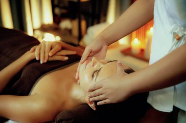 Beyaz kadın stres önleyici kafa masajı yapmaktan ve lüks otel veya otelde sıcak mum ışığında yüz güzelliği eğlencesi yapmaktan zevk alıyor. Sessiz.