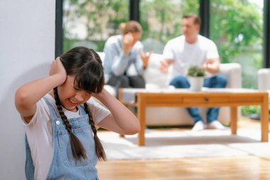 Stresli ve mutsuz kız köşede toplanır, ailesi arka planda tartışırken kulaklarını acılı bir ifadeyle kapatır. Aile içi şiddet ve travmatik çocukluk depresyona dönüşür. Eşzamanlama