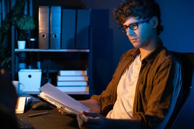 Genç işadamı, Neon Light Modern Ofis 'teki yeni proje surround çalışma masası için kağıt üzerinde tasarım düşünüyor. E-posta ile hediye göndermeden önce not defterine yeni bir iş düşünüyorum. Toplayıcı.