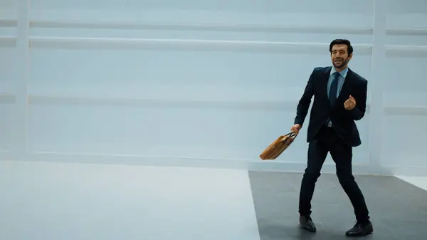 Professional project manager dancing to celebrate success project while moving to lively music with white background. Skilled business man holding bag while dancing. Motion shot. Copy space. Exultant.