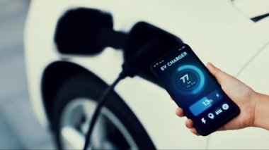 Akıllı telefon ekranı akıllı EV mobil uygulama üzerinde pil durumu EV araba garajdaki ev şarj istasyonu ile elektrik şarj ederken. Geleceğin yenilikçi EV arabası ve enerji sürdürülebilirliği. İnceleyin