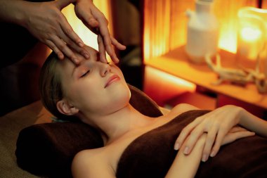 Beyaz kadın stres önleyici kafa masajı yapmaktan ve lüks otel veya otelde sıcak mum ışığında yüz güzelliği eğlencesi yapmaktan zevk alıyor. Sessiz.