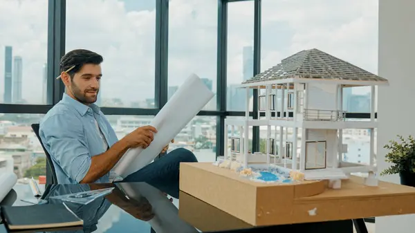 Uśmiechnięty Inżynier Patrząc Plan Projektu Podczas Projektowania Modelu Domu Biurze — Zdjęcie stockowe