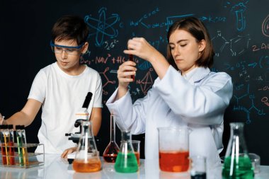 Öğretmen, laboratuarda öğrenciyi destekliyor. Öğrenci ve öğretmen cam kapta sıvı kullanarak STEM sınıfında kimya bilimi üzerine deney yapıyorlar. Karıştırma çözeltisi. Etkinlik.