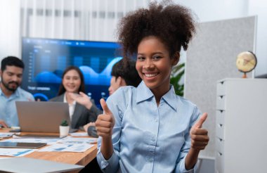 Bir grup ofis çalışanı ile birlikte arka planda ekranda gösterim paneliyle buluşan mutlu Afrikalı genç bir iş kadını portresi. Takım toplantısında kendine güveni tam bir ofis hanımı. Uyum