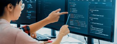 Kadın programcı bilgisayarda gösterilen kodu işaret ederken açıklıyor. Profesyonel programcı modern şirket ofisinde veri analizi ve Java betiği sunar. - Yakın çekim. Filizlenen.