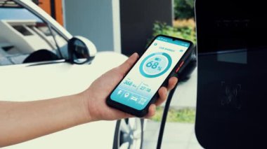 Akıllı telefon ekranı akıllı EV mobil uygulama üzerinde pil durumu EV araba garajdaki ev şarj istasyonu ile elektrik şarj ederken. Geleceğin yenilikçi EV arabası ve enerji sürdürülebilirliği. İnceleyin