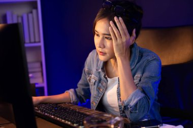 Stresli, genç, güzel Asyalı yaratıcı proje yaratıcısı sosyal medyayı araştırmak için bilgisayara bakıyor ve geceleri daha çok neon modern ofisin planlama kanalı stratejisine ulaşılıyor. Taktik.