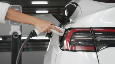 Genç adam EV elektrikli arabasıyla şehir merkezindeki alışveriş merkezinin otoparkına gidiyor şehir merkezindeki sürdürülebilirlik yaşam tarzını yeşil, temiz, yeniden şarj edilebilir elektrikli araç iç organlarıyla şarj ediyor.