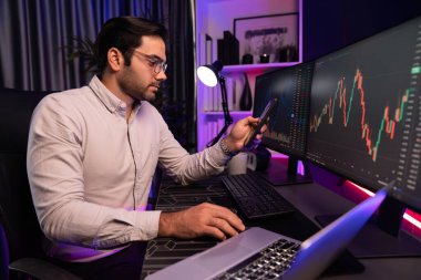 Akıllı tüccar akıllı iş adamı akıllı telefonu kullanarak modern evde kâr amaçlı finans teknolojisi ile neon ışık ofisindeki bilgisayarda dinamik borsa yatırımlarını araştırır ve analiz eder. Tahmin et..