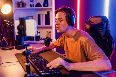 Oyun kanalı, online oyun oynayan akıllı flamalı oyun sunucusu, kulaklık takan, neon ışıklandırma odasındaki takım oyuncusuyla akıllı telefondan canlı yayında konuşan izleyiciler. Bireysel.