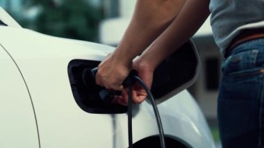 Adam evdeki şarj istasyonundan elektrikli arabasını EV şarj cihazıyla şarj ediyor. EV arabaların teknolojik gelişimi ve gelecekteki sürdürülebilir enerji için ev enerjisi altyapısı. İnceleyin