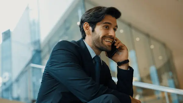Smart business man calling phone to manager while discuss about business plan. Skilled executive manager talking to phone with blurred background. Successful investor smiling while sitting. Exultant.