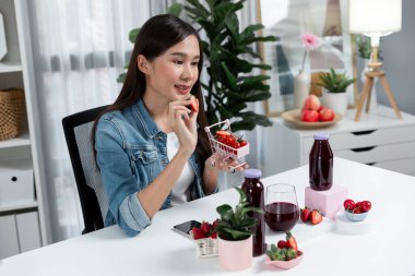 Gülümseyen, güzel Asyalı genç, lezzetli karışık çilek ve kiraz suyu detoksu içeceklerini inceleyen, sosyal medyada özel promosyon satışı için sağlıklı ürünler sergileyen. Taktik.