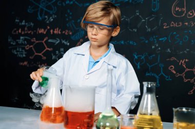Laboratuvardaki sarışın çocuk laboratuvar önlüğü giyer ve STEM sınıfında kimya bilimi öğrenir. Öğrenci cam şişeye sıvı döker. Masaya bir sürü şişe koy. Etkinlik.
