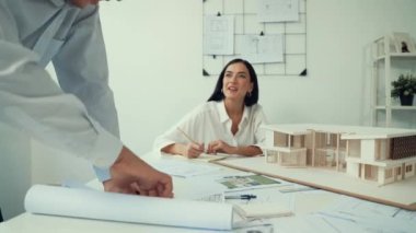 Ev modeliyle çalışan yetenekli beyaz tasarımcı Asyalı mimar mühendis ile toplantı masasında üzerinde taslak ve ev modeli dağınıklığı olan ev planlarını tartışırken. Tertemiz..