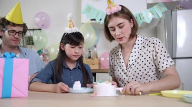 Kafkasyalı anne doğum günü pastasını kesiyor ve babaya verirken tatlıyı ayırıyor. Mutlu aile, kızının doğum gününde masada otururken parti şapkası takar. Özel durum konsepti. Pedagoji.