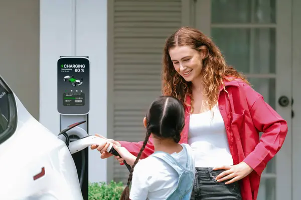 幸せな小さな少女は 母親がEv充電ステーションから電気自動車を充電するのを助けるため 環境にやさしいエネルギーの持続可能性について学びます Evカーとモダンなファミリーコンセプト シンクロノス — ストック写真