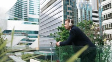 Kulaklıklı yönetici çatıda dururken müzik dinlemekten zevk alır. Rahatlamış yatırımcı kulaklık takıyor ve modern gökdelen manzarasına bakarken kafiyeli müzik çalıyor. Yaşam tarzı. Urbane.