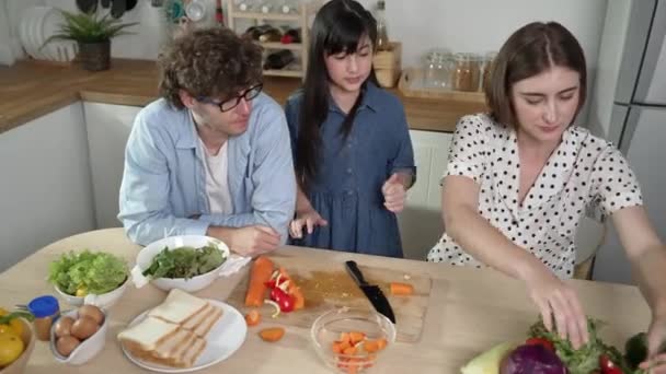 アジアの娘と新鮮な食事を調理するために 魅力的な白人のお父さんと母親は一緒に時間を過ごします エネルギッシュなパパとママは キッチンでサラダを作るために新鮮な野菜を準備しています 健康的な食べ物 ペダゴロジー — ストック動画