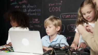 Çocuğun dizüstü bilgisayar mühendisliği kodunu ve yazım programını kullanırken bir grup zeki öğrencinin etrafı STEM teknoloji sınıfında arkadaşlarıyla çevriliyken karatahtaya oturması. Etkinlik.