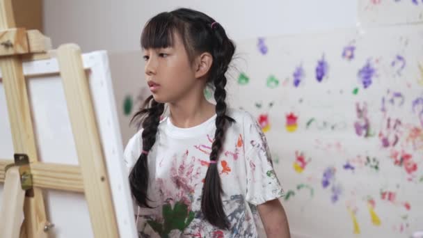 芸術レッスンでステンドウォールで遊び心のある学生が描いた または描いたキャンバス アジアの少女は 手のプリントでステンドウォールに立っている間 染色された色の白いシャツを着ています クリエイティブ活動 エラー — ストック動画