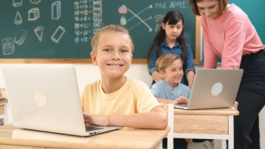 Beyaz çocuk çeşitli öğrenci kodlama mühendisliği komut ile çevrili kameraya bakarken programlama sistemine odaklanıyor. Happy öğretmen bilgisayar dersinde dizüstü bilgisayarda çalışan çocuklara destek oluyor. Pedagoji.