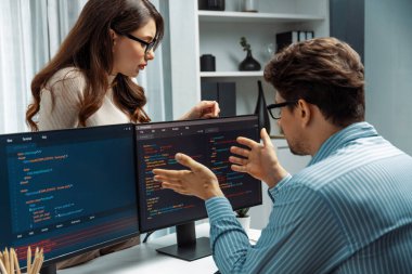 Masada çalışan erkek programcının karşısında duran kadın meslektaşım iki bilgisayar ekranında kodlama web sitesi yazılım sistemi projesini tartışmak için tam yığın veri dizaynı ile karşılaştırıyor. Varsayım.