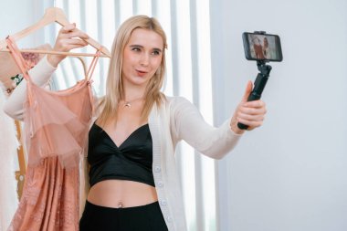 Genç sosyal medyum kadın moda videosu yapıyor. Blogcu gülümseyip telefon çubuğu selfie 'si kullanırken aynı zamanda ikna edici online giysiler izleyicilere ya da takipçilere vlog sattırıyor. Blithe