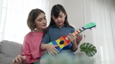 Kafkasyalı bir anne evde akustik müzik öğretirken ukulele çalan mutlu kız. Sevimli çocuk enstrüman öğreniyor. Kafkasyalı mutlu anne ve kız birlikte vakit geçiriyorlar. Pedagoji.
