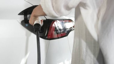Genç hareketli kadın, EV elektrikli arabasıyla şehir merkezindeki alışveriş merkezinin otoparkına gidiyor. Sürdürülebilirlik yaşam tarzını yeşil, temiz, yeniden şarj edilebilir elektrikli araç iç organlarıyla şarj ediyor.