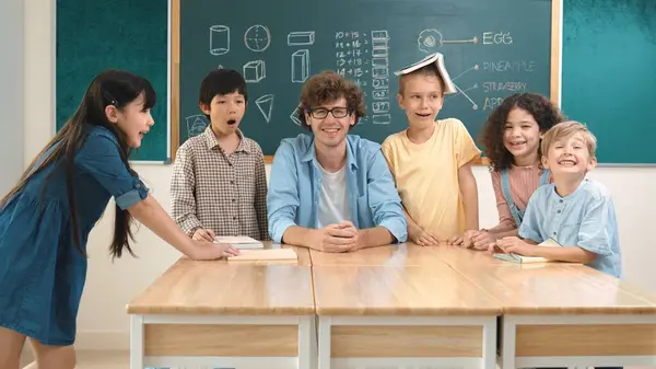 Professional caucasian teacher and diverse student looking at camera while happy school boy smiling. Group of multicultural children smiling while standing in front of classroom. Education. Pedagogy.
