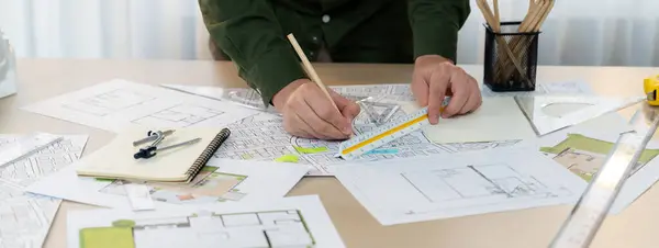 A portrait of architect using divider to measure blueprint. Architect designing house construction on a table at studio, with architectural equipment scattered around. Focus on hand. Delineation