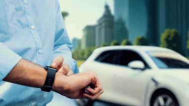 İş adamı, ESG yeşil parktan akıllı saat hologram şarj şarjının EV araba aküsü durumunu kontrol et. Modern şehir yaşam tarzı ve karbondioksiti azaltmak için çevre dostu elektrikli araba kullanımı. İnceleyin