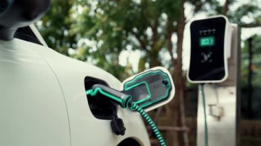 Doğal yeşil araba parkındaki ekolojik temiz enerji şarj istasyonundan gelen fütürist akıllı EV şarj aletinin şarj ettiği elektrikli araba. Alternatif enerji kullanan gelecekçi çevre dostu elektrikli araba. İnceleyin