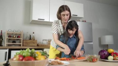 Zeki beyaz anne ve Asyalı kız birlikte yemek pişiriyor ve sebze doğruyor ya da akşam yemeği için salata hazırlıyor. Mutlu anne ve kız taze yemekle sağlıklı yemek yapıyorlar. Sağlıklı gıda konsepti. Pedagoji.