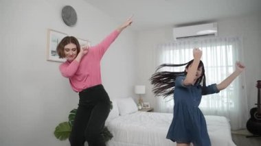 Yatak odasında Asyalı kızıyla müzik eşliğinde dans eden mutlu çekici anne. Beyaz anne dans eder ya da egzersiz yapar. Bu arada tatlı çocuk da müzik eşliğinde yatağa atlar. Aile eğlence konsepti. Pedagoji.