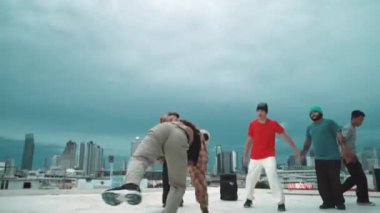 Profesyonel hippi hareketsiz poz verirken aynı zamanda şehir manzaralı çatıdaki müziğe ayak basıyor. Break dansçı, hip-hop dansçıları grubuyla birlikte sokak dansı yapıyor. Açık hava sporu 2024 hiphop..